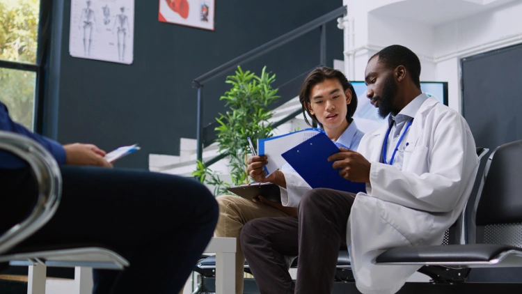 two-people-sit-room-one-them-is-wearing-white-lab-coat-other-is-holding-papers-other-is-holding-clipboard-with-word-health-it